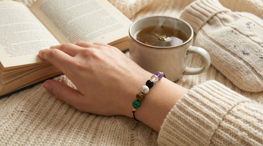 Pain relief support gemstone bracelet styled beside a heat pack, journal and cup of tea on a soft, neutral surface
