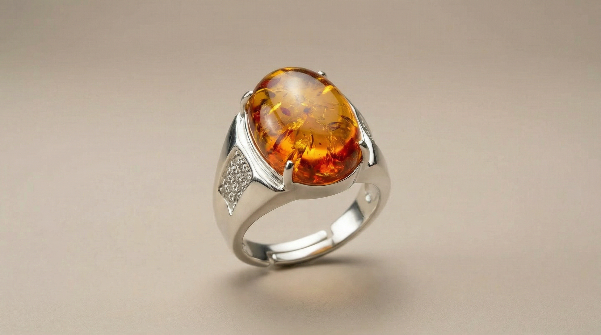 Amber statement ring with prong-set oval cabochon and pavé-style side accent, photographed on a soft neutral background.