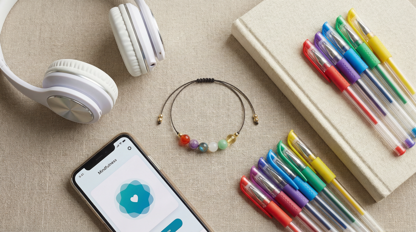 Teen support gemstone bracelet styled beside notebooks, headphones and a phone on a desk