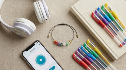 Teen support gemstone bracelet styled beside notebooks, headphones and a phone on a desk