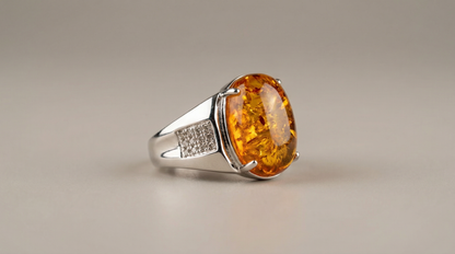 “Polished silver-tone ring with oval amber cabochon centerpiece and pavé-style side accent on neutral background.”